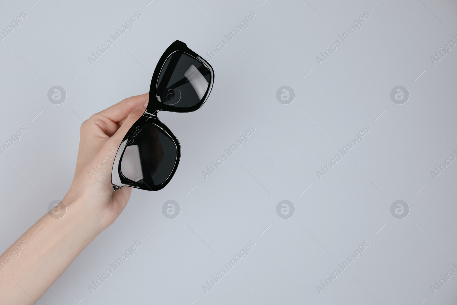 Photo of Woman holding stylish sunglasses on light background, closeup. Space for text