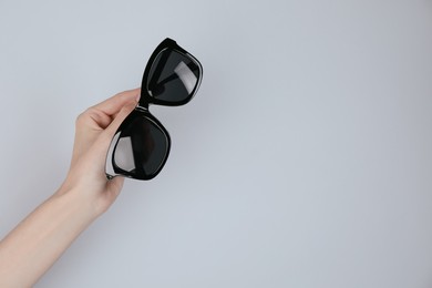 Woman holding stylish sunglasses on light background, closeup. Space for text