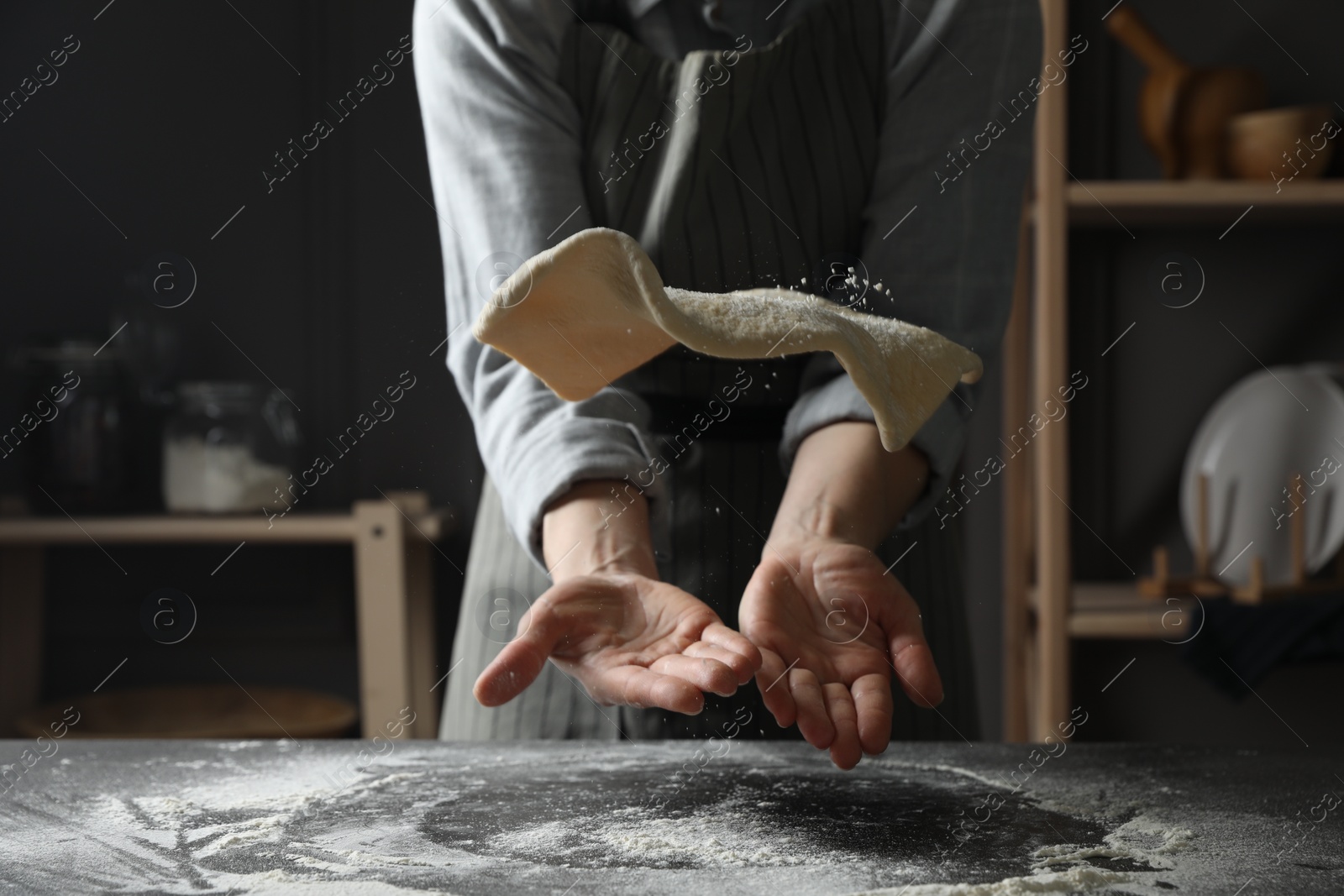 Photo of Woman tossing pizza dough at table in kitchen, closeup