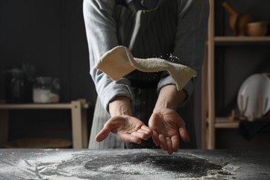 Photo of Woman tossing pizza dough at table in kitchen, closeup