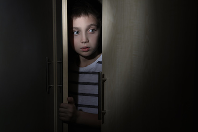 Photo of Scared little boy hiding in wardrobe. Domestic violence concept