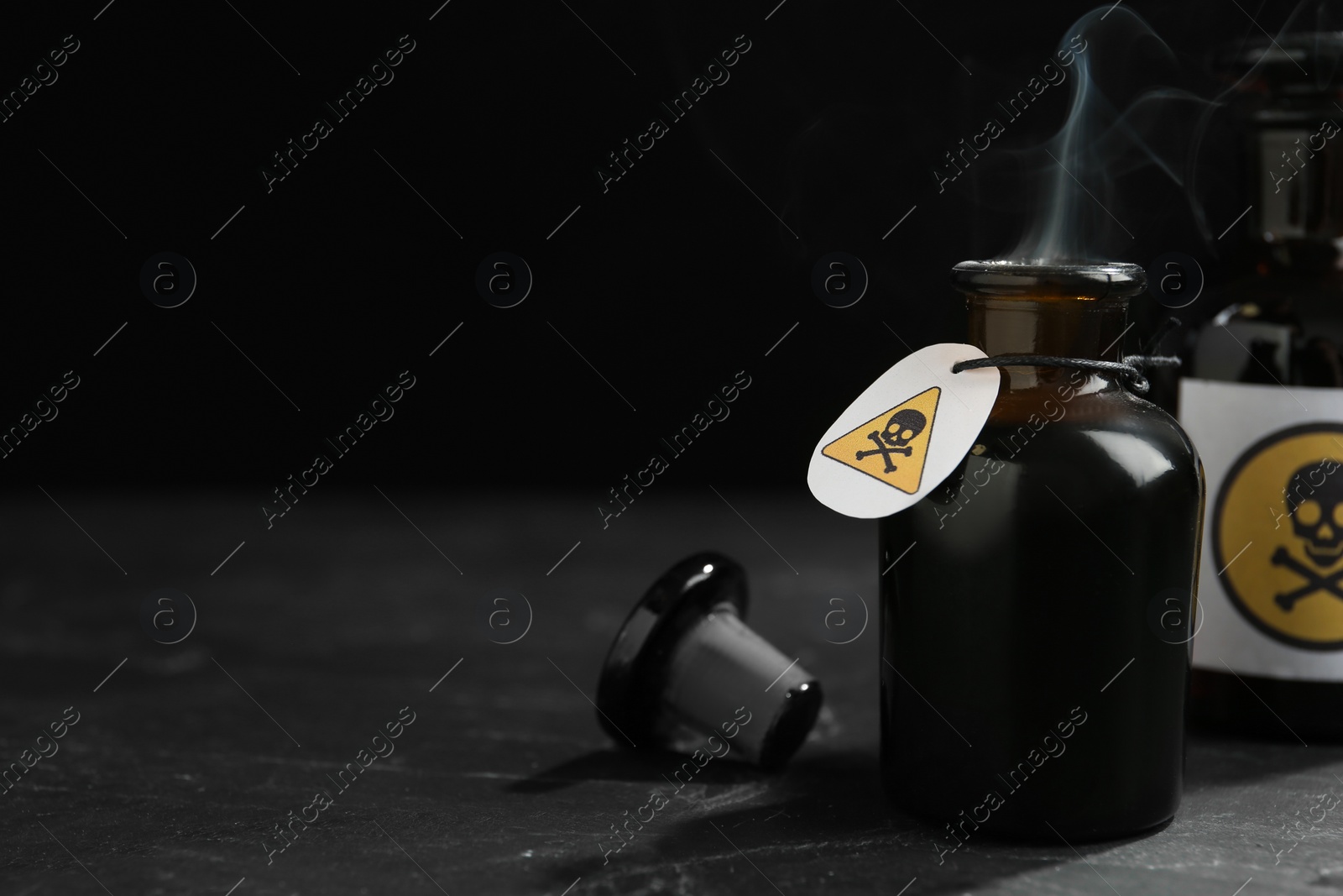 Photo of Open glass bottle of smoking poison with warning sign on black table. Space for text