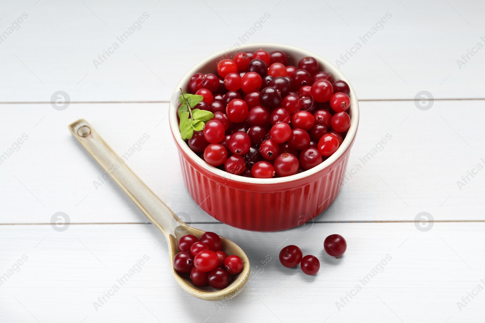 Photo of Fresh ripe cranberries in bowl and spoon on white wooden table, closeup