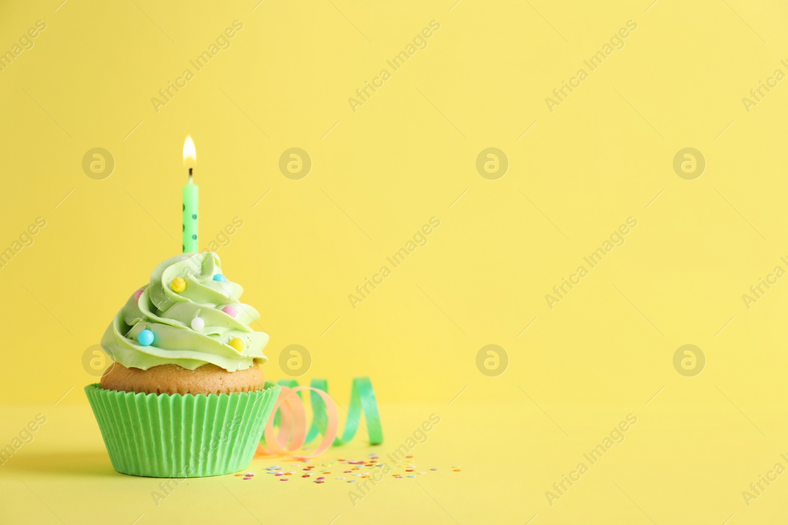 Photo of Delicious birthday cupcake with burning candle, sprinkles and streamers on yellow background, space for text