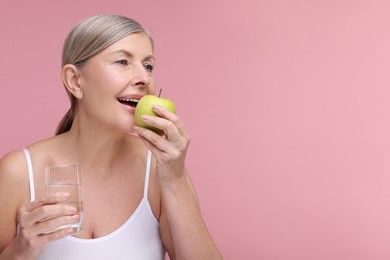 Photo of Beautiful woman with glass of water eating fresh apple on pink background, space for text. Vitamin rich food