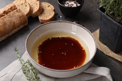 Photo of Bowl of balsamic vinegar with oil, spices and bread on dark grey table