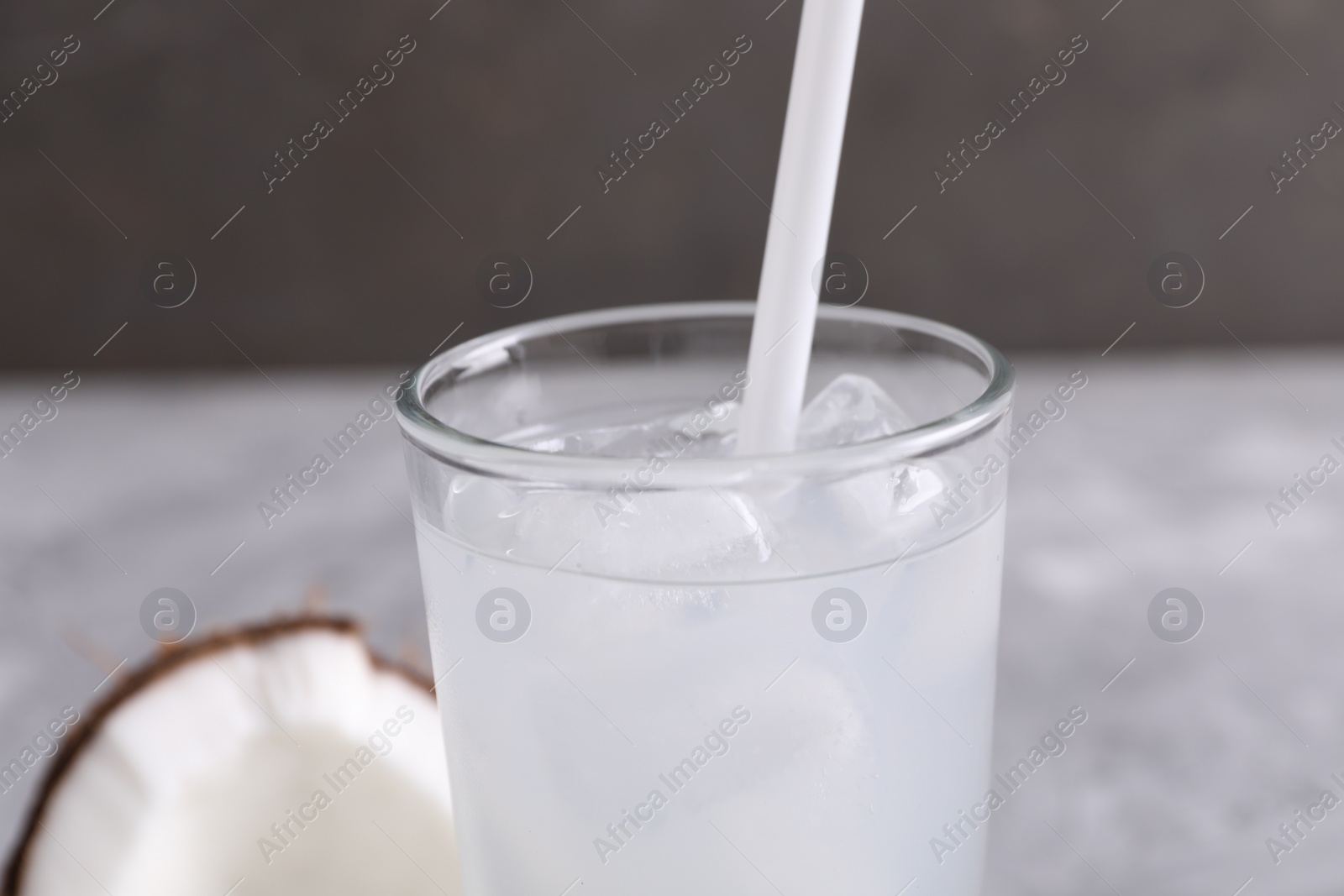 Photo of Glass of coconut water with ice cubes on grey table, closeup