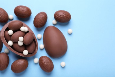 Photo of Delicious chocolate eggs and candies on light blue background, flat lay. Space for text