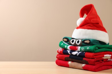 Photo of Stack of different Christmas sweaters and Santa hat on table against beige background. Space for text