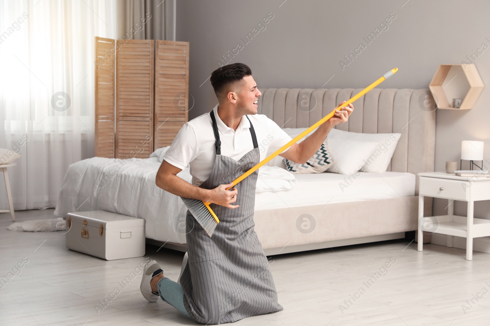 Photo of Man with mop singing while cleaning in bedroom