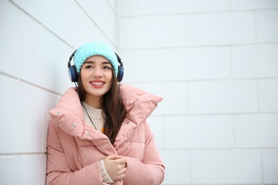 Photo of Beautiful young woman listening to music with headphones near light wall. Space for text