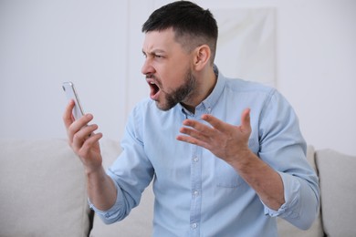 Photo of Emotional man with smartphone at home. Online hate concept