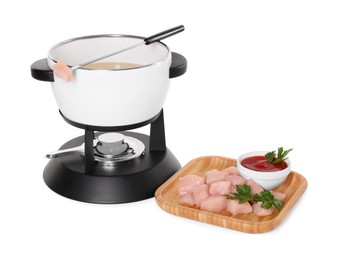 Photo of Oil in fondue pot, fork, pieces of raw meat and sauce isolated on white