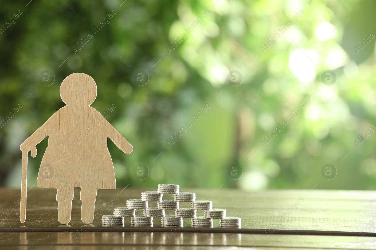 Photo of Pension savings. Figure of senior woman and stacked coins on wooden table outdoors, space for text