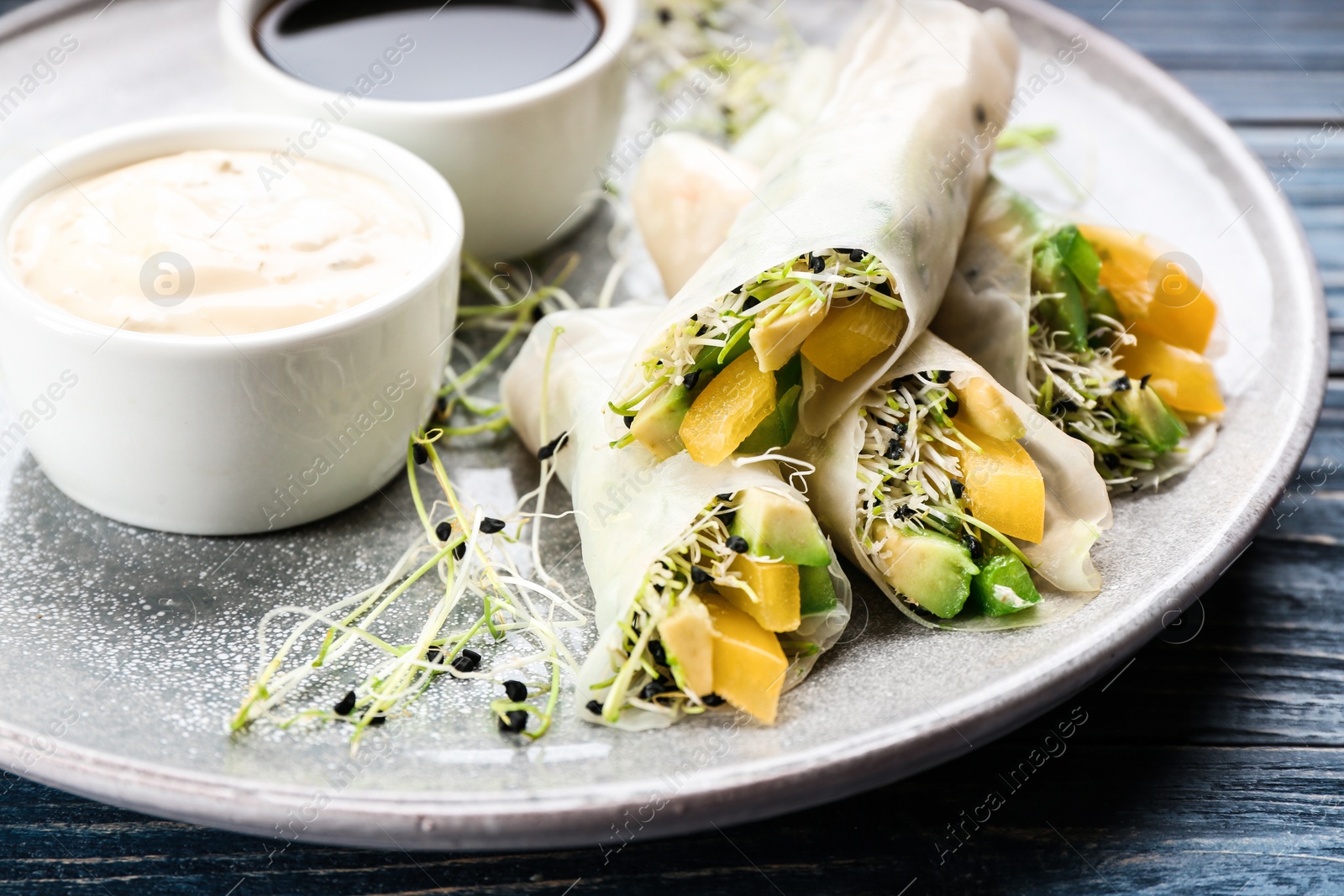 Photo of Delicious rolls wrapped in rice paper served on blue wooden table, closeup