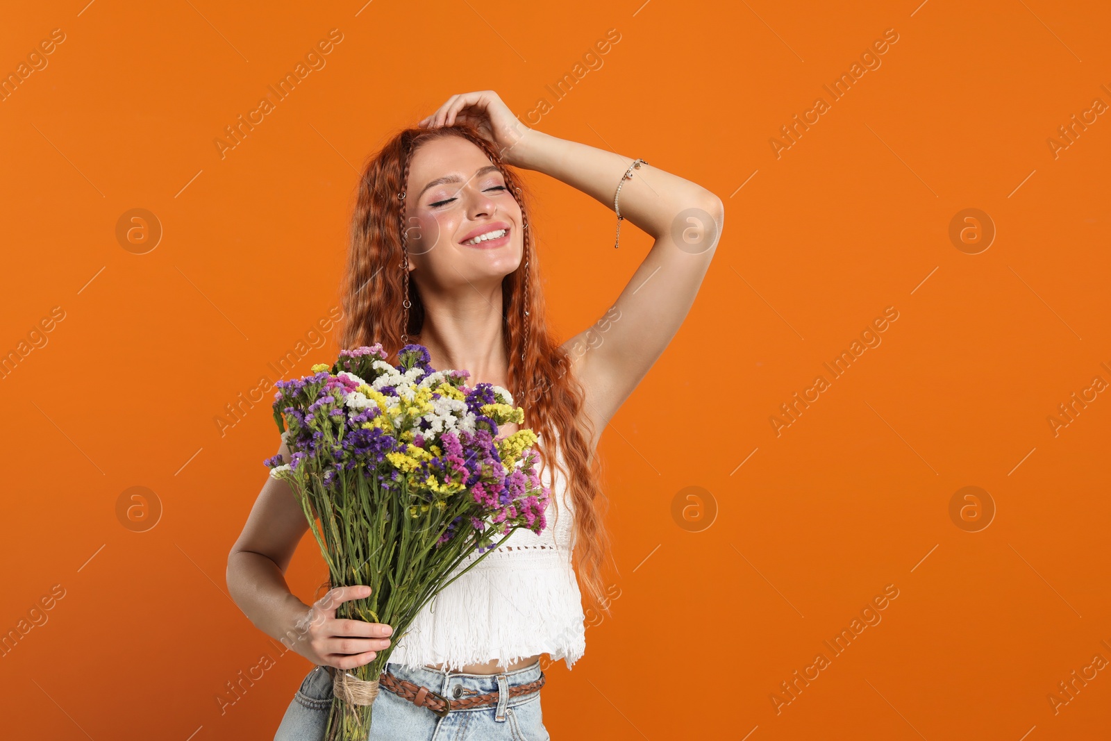 Photo of Beautiful young hippie woman with bouquet of colorful flowers on orange background, space for text