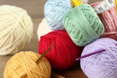 Photo of Many different clews of colorful knitting threads, measuring tape and crochet hooks on wooden table, closeup