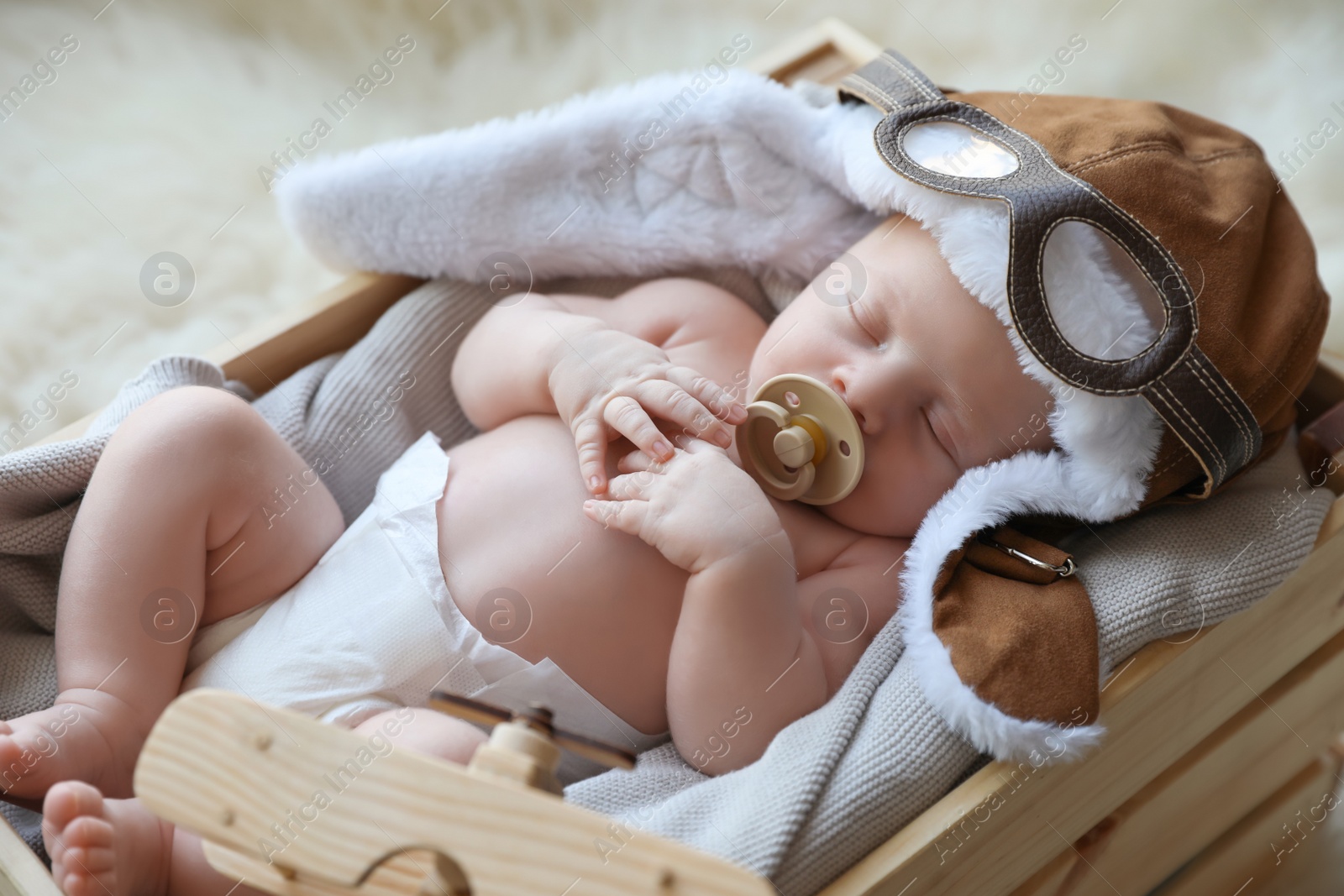 Photo of Cute newborn baby wearing aviator hat with toy sleeping in wooden crate