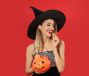 Beautiful woman wearing witch costume with Jack O'Lantern candy container on red background, space for text. Halloween party