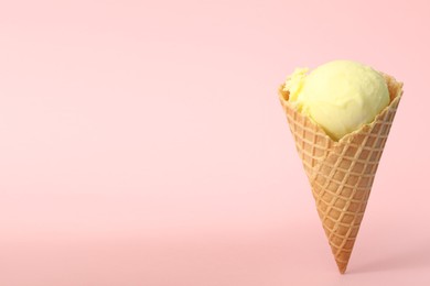 Photo of Delicious yellow ice cream in waffle cone on pink background. Space for text