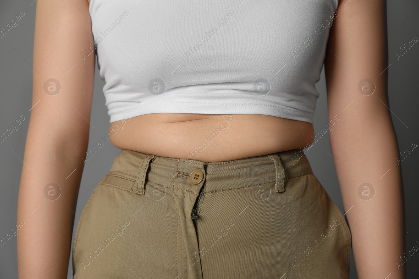 Photo of Overweight woman in tight pants on grey background, closeup