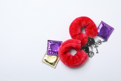 Furry handcuffs and condoms on white background, top view. Sex game