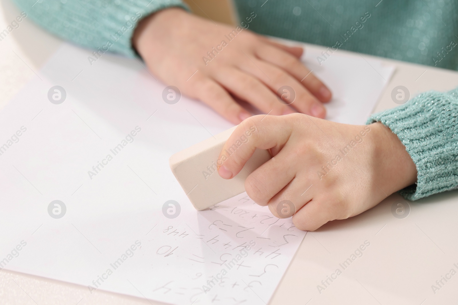 Photo of Girl erasing mistake in her homework at white desk, closeup