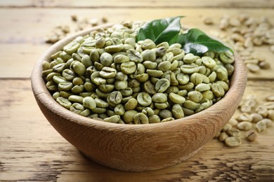 Photo of Green coffee beans and leaves in bowl on wooden table, closeup