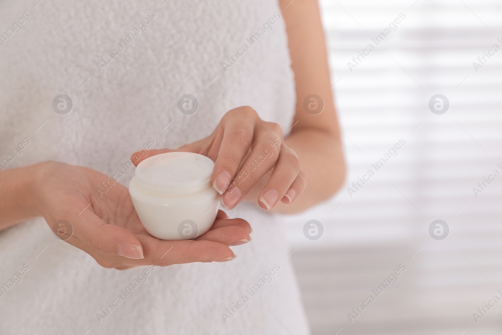 Photo of Woman holding jar with cream near window, closeup