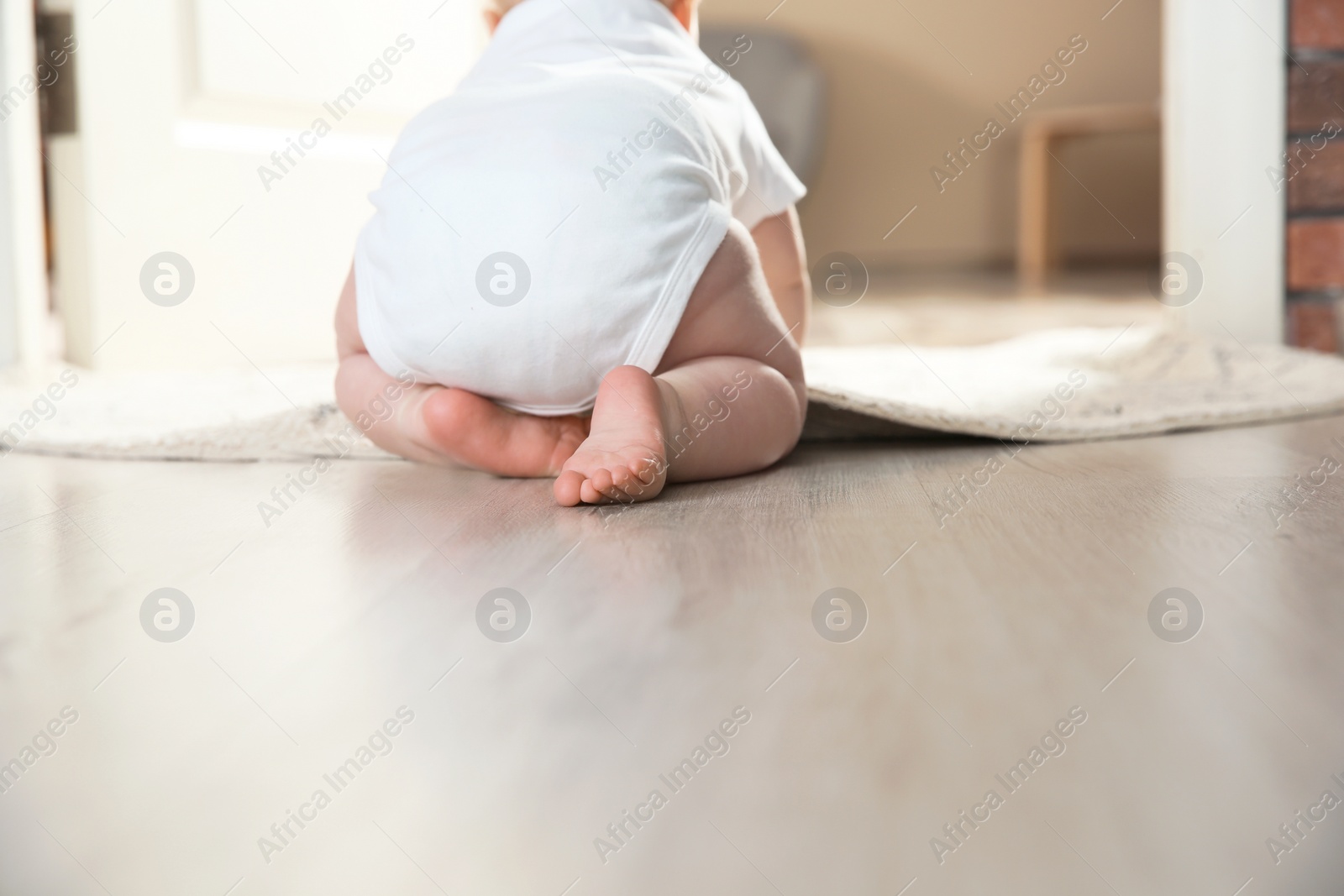 Photo of Cute little baby crawling on floor indoors, closeup