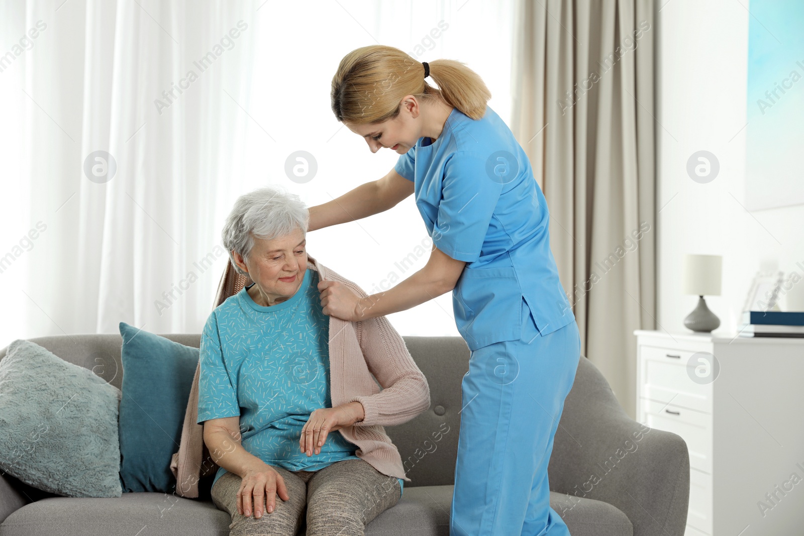 Photo of Nurse covering elderly woman with blanket indoors. Assisting senior people
