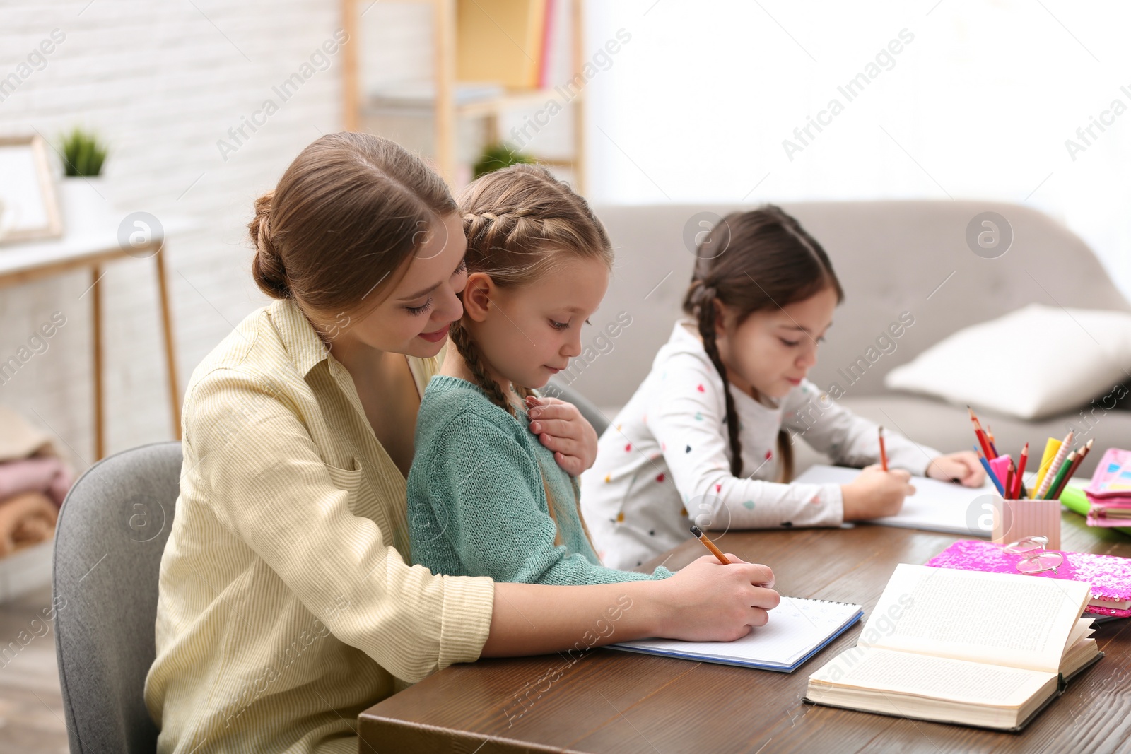 Photo of Mother helping her daughters with homework at table indoors