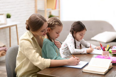 Mother helping her daughters with homework at table indoors