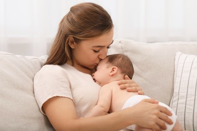 Mother kissing her cute newborn baby on sofa indoors