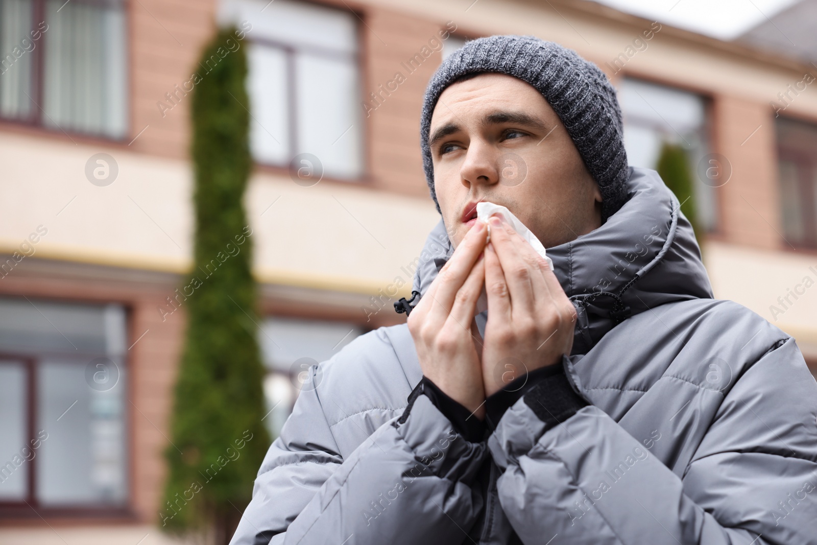 Photo of Sick young man with tissue on city street. Cold symptoms