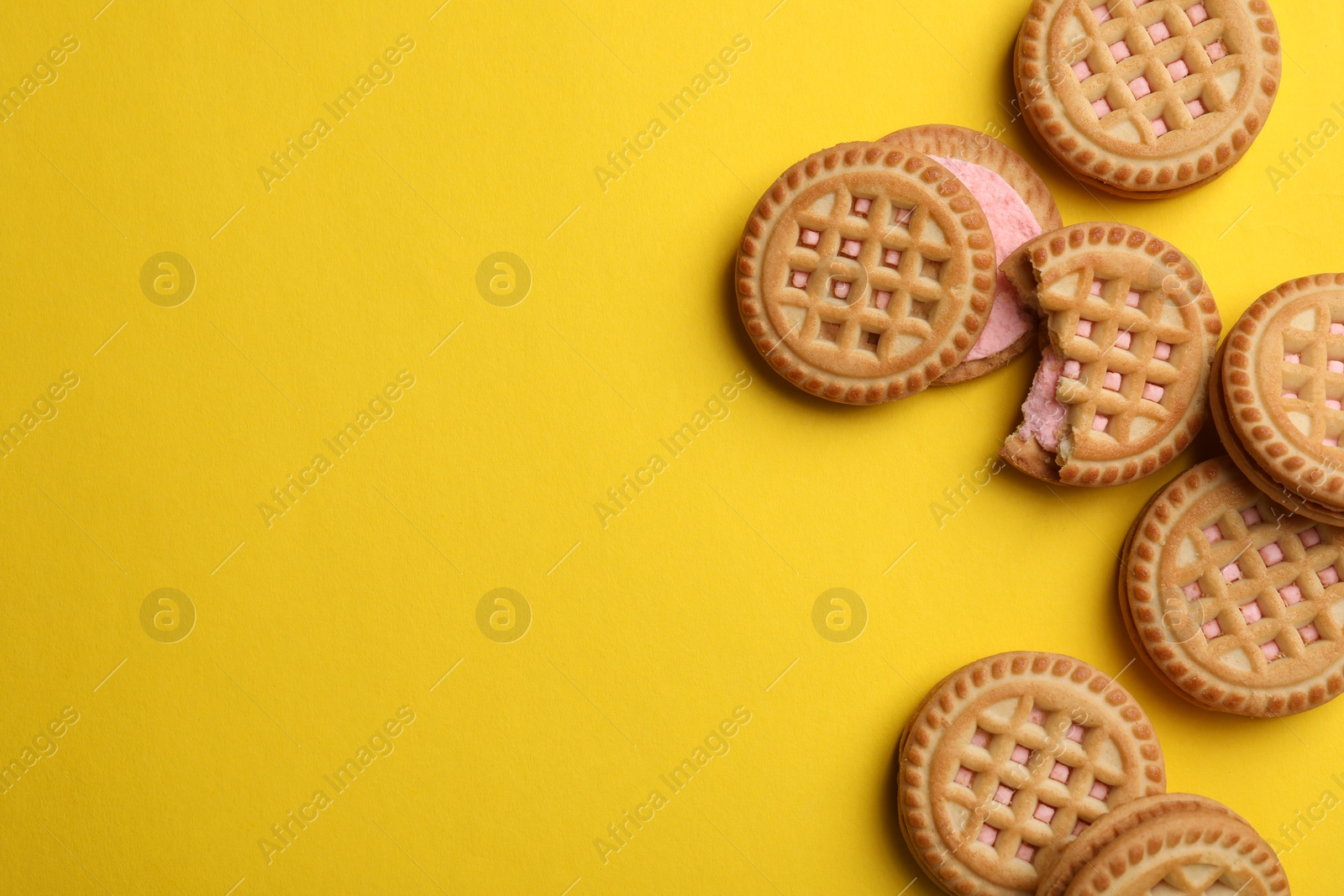 Photo of Tasty sandwich cookies with cream on yellow background, flat lay. Space for text