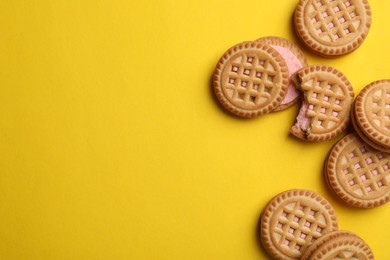 Tasty sandwich cookies with cream on yellow background, flat lay. Space for text