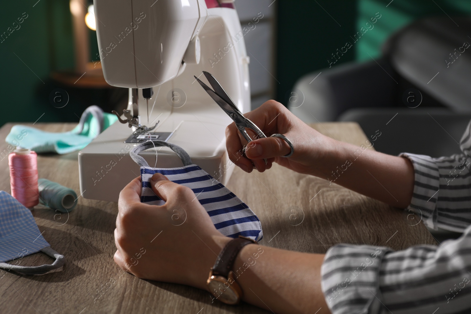Photo of Woman sewing cloth protective mask with machine and scissors at table indoors, closeup