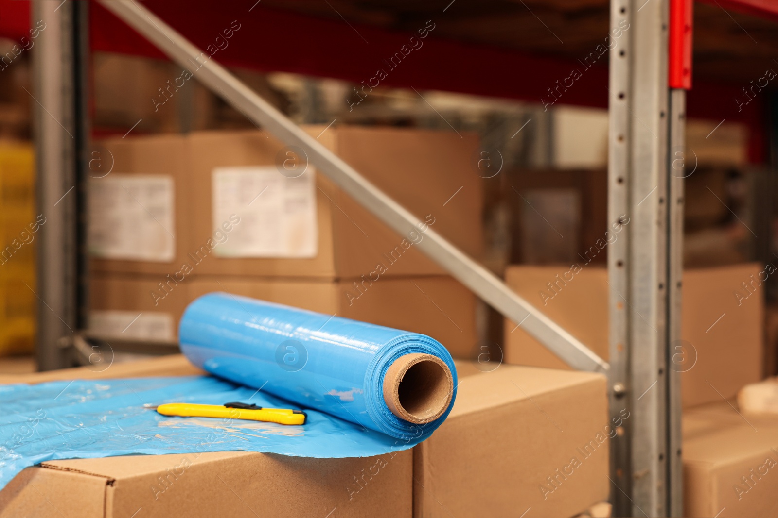 Photo of Roll of stretch wrap and utility knife on boxes in warehouse