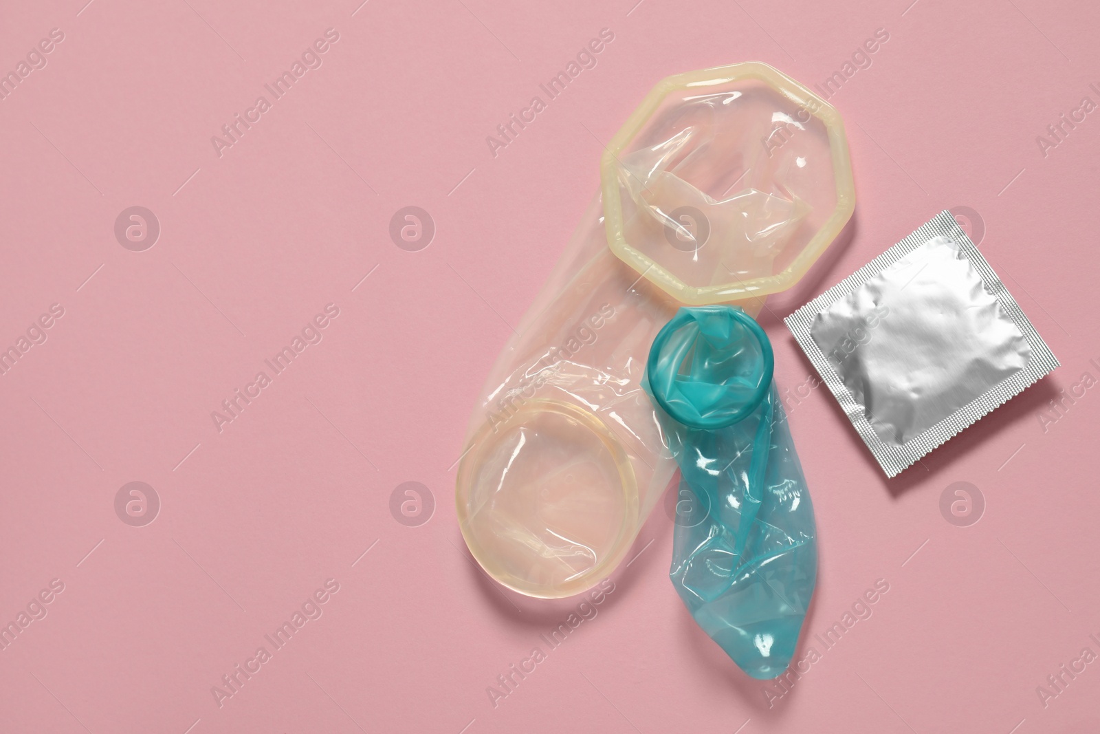 Photo of Unrolled female and male condoms with package on light pink background, flat lay with space for text. Safe sex