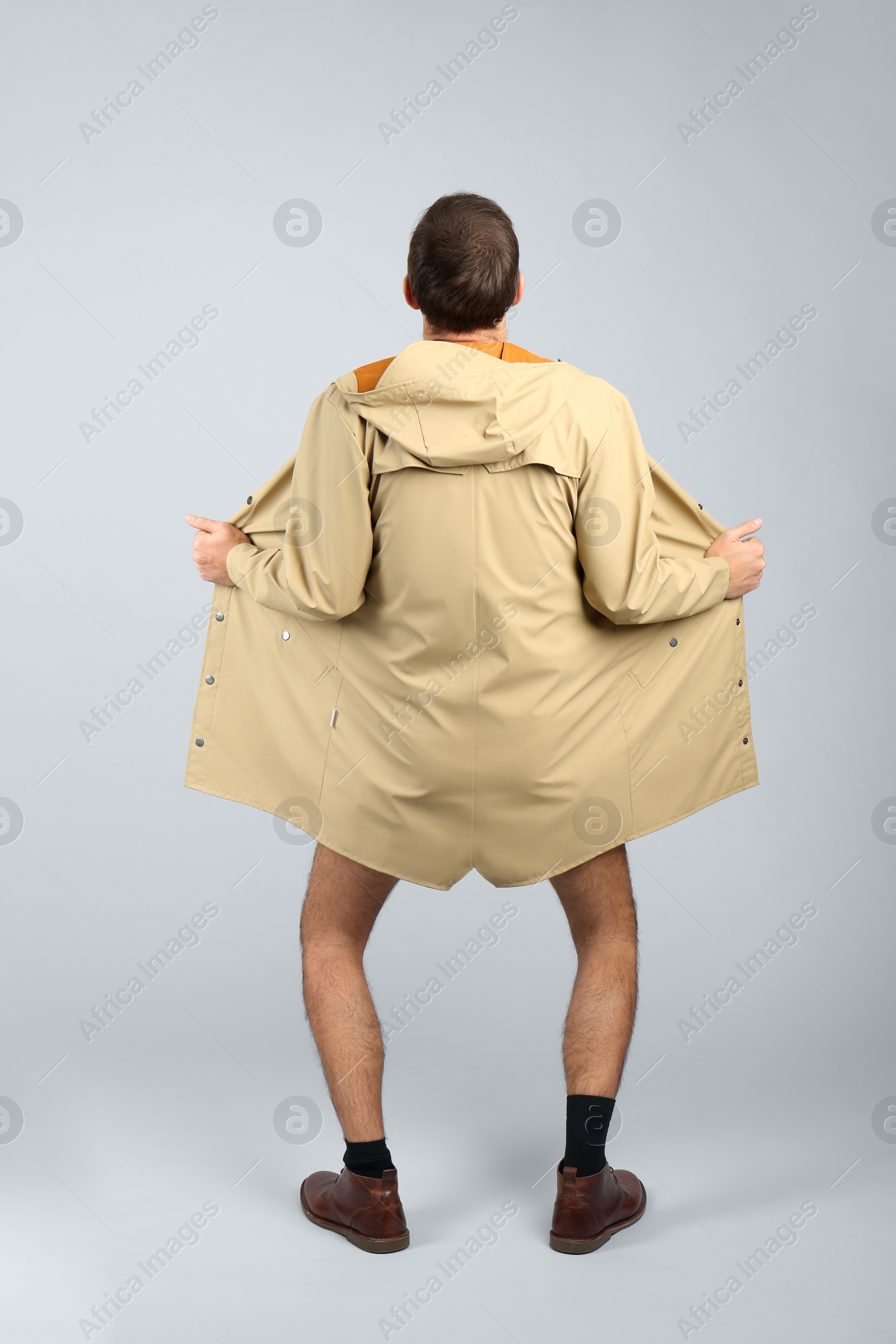 Photo of Exhibitionist exposing naked body under coat on light background, back view