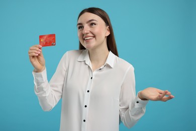 Happy woman with credit card on light blue background