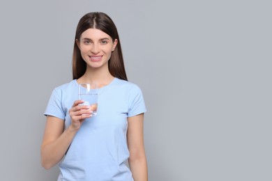 Healthy habit. Portrait of happy woman holding glass with fresh water on grey background. Space for text