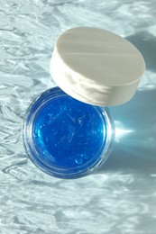 Photo of Open jar of cosmetic product on light blue background, top view