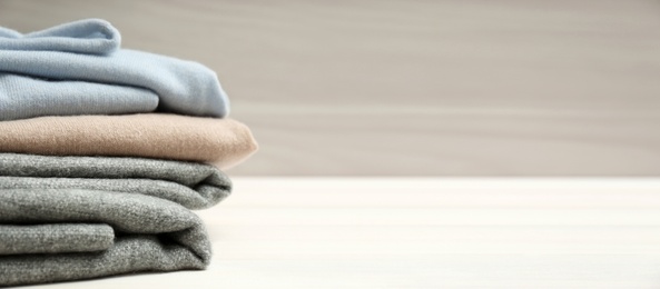 Image of Stack of cashmere clothes on wooden table, space for text. Banner design