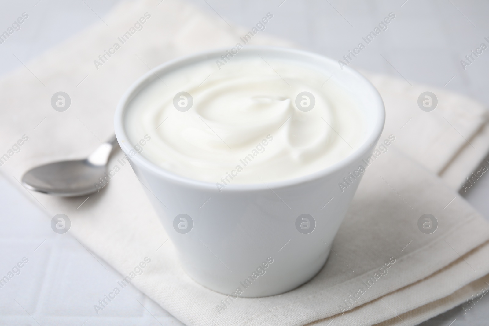 Photo of Delicious natural yogurt in bowl and spoon on white table, closeup