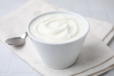 Delicious natural yogurt in bowl and spoon on white table, closeup