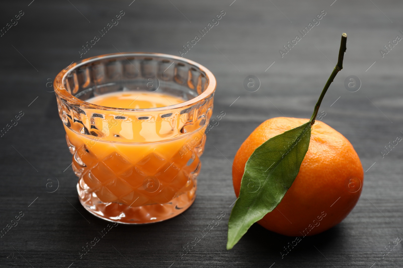 Photo of Tasty tangerine liqueur in glass and fresh fruit on black wooden table, closeup