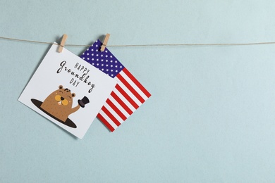 Photo of Happy Groundhog Day greeting card and American flag hanging against light background, space for text