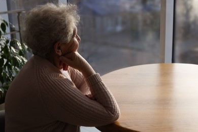 Photo of Elderly woman looking out of window on rainy day, space for text. Loneliness concept